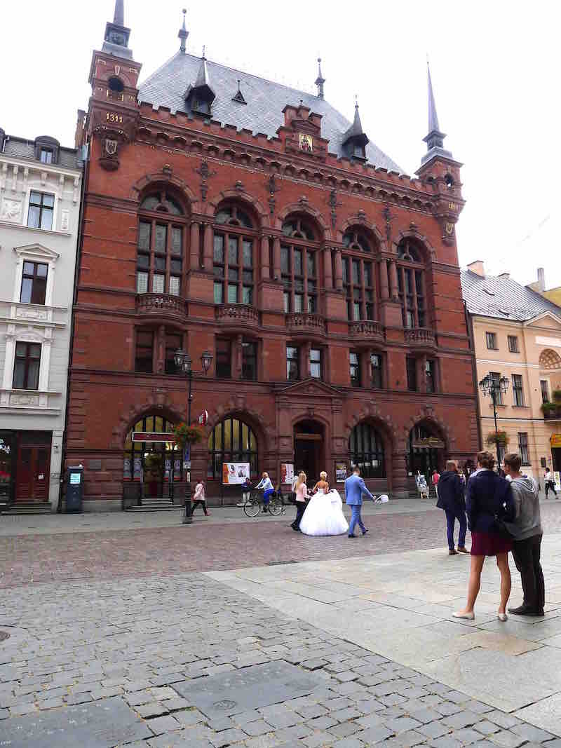 Rood bakstenen gebouw met stel in bruidskleding er voor